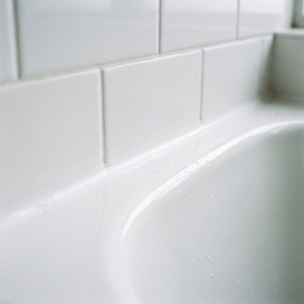 Clean white caulk line sealing the gap between a bathtub and tile wall