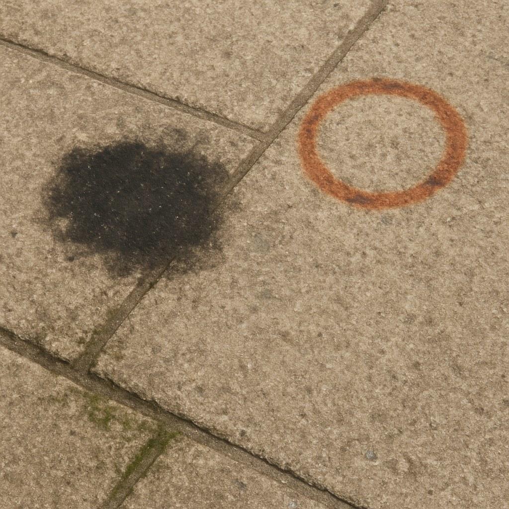 A patio surface made of pavers showing various stains including oil, rust, and mildew.